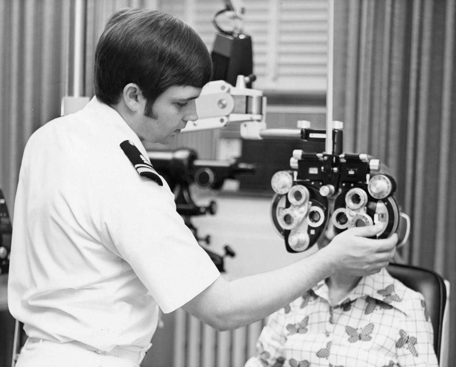 An optometrist examines a patient's eyes with a phoropter.